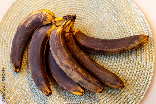 A bunch of nearly overripe bananas with blackened tips lies on a pale green napkin on the table.