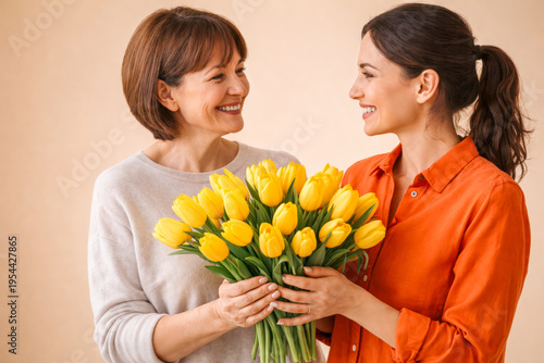 Adult daughter giving yellow tulips bouquet to senior mother