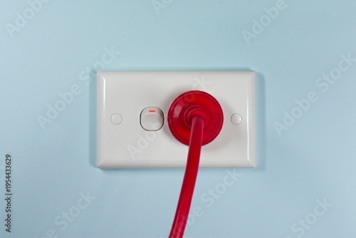 Closeup of a red Australian electricity cord plugged into a power socket outlet. This electrical power cable illustrates the concept of expensive energy and bill cost savings.