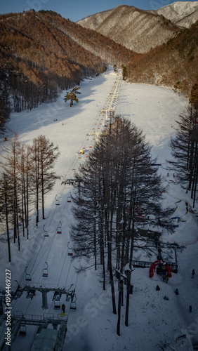 A wide panoramic view of the snowy ski slopes and chairlifts at Bandai Plateau, Hotel Listel Inawashiro, surrounded by magnificent mountains in Japan.