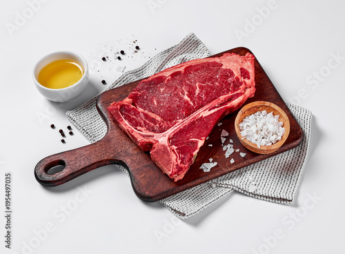 Tableau sur toile Raw T-bone beef steak on wooden cutting board with salt and oil