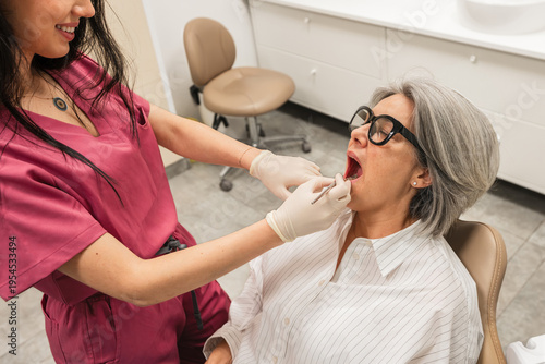 Schilderij op canvas Dentist performing a routine check up on an elderly woman's teeth and gums, focu