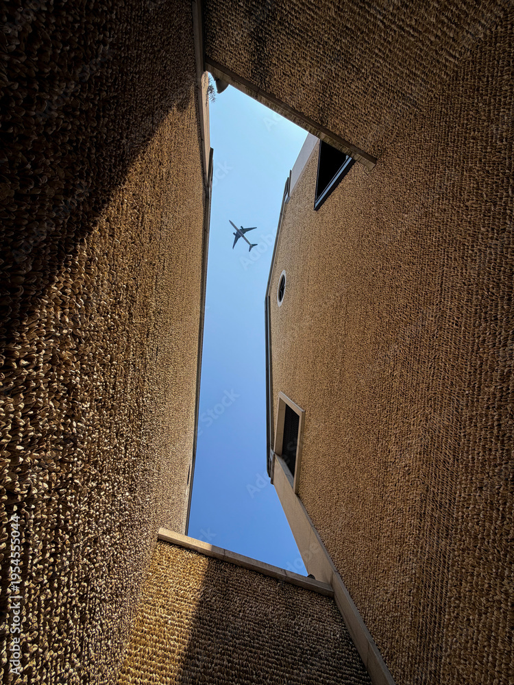Obraz premium Plane overhead between textured building walls