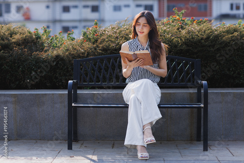 Fotografi Young asian woman reading book on park bench