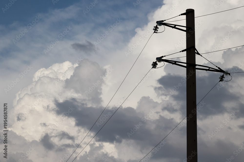 Fototapeta premium Electricity pylon silhouette against dramatic white cumulus clouds