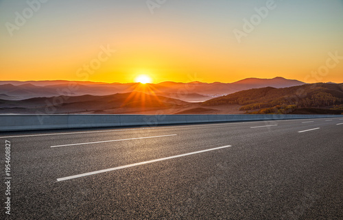 Empty asphalt highway through dramatic mountain landscape at sunrise, transportation and logistics concept, copy space.