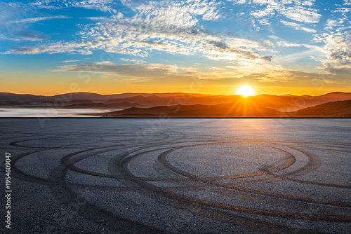 Empty asphalt road with tire skid marks against scenic mountain background at sunset. Automotive performance and drifting concept.