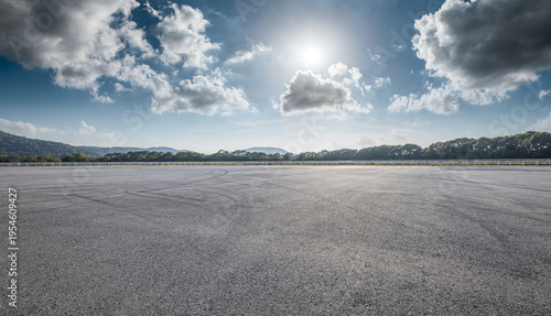 Large empty asphalt parking lot with tire marks under blue sky for commercial display.