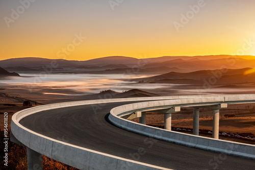 Curved concrete highway bridge overpass overlooking a misty valley landscape during a beautiful golden sunset in China.