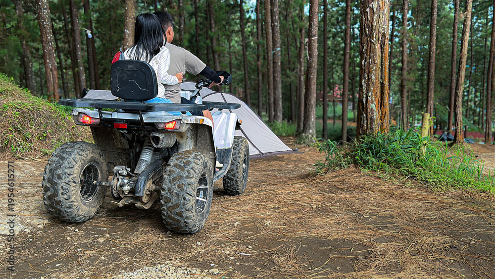 Fototapeta premium a young boy and girl riding an all-terrain vehicle (ATV) along a dirt path in a lush pine forest.
