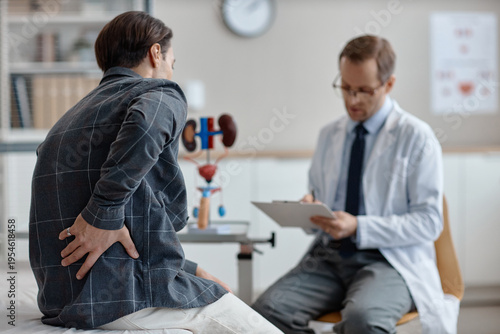 Fotografía Middle aged Caucasian man sitting on examination table, holding lower back while