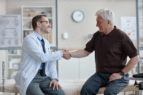 Quadro su tela Middle aged Caucasian male doctor wearing glasses shaking hands with senior Cauc
