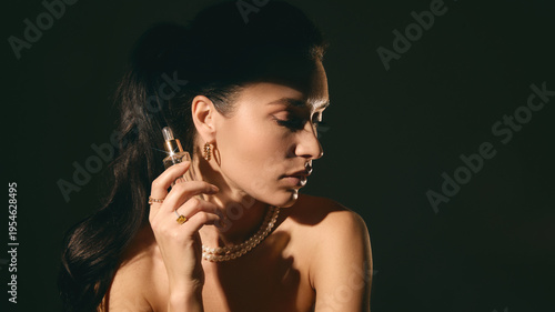 Woman applying serum with dropper bottle in moody lighting studio portrait. Concept of skincare routine, cosmetic application, beauty care and premium product advertising.
