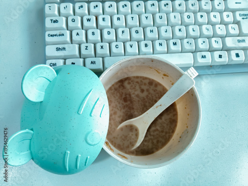 Top View of Kids Bowl with Spoon and Milk Breakfast on Office Desk with Keyboard
