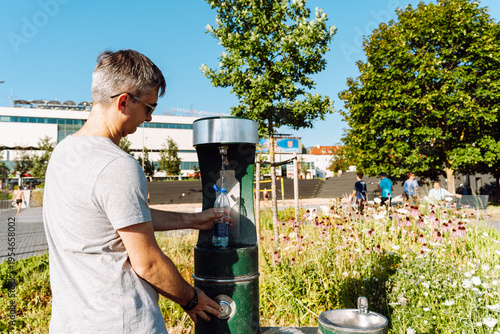 Fotografie Man filling water bottle at public drinking fountain outdoors