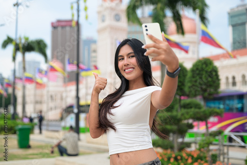 Thai Woman at Merdeka Square Kuala Lumpur using phone in front of the Sultan Abdul Samad Building.