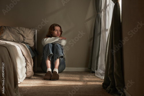 Canvas Print Caucasian teenage girl sitting on floor near bed hugging knees appearing thought