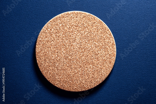 Circular brown cork coaster isolated on a dark navy blue textured background, providing a clean top-down perspective for branding.