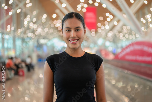 A portrait of a smiling young Asian woman wearing a black t-shirt in a modern airport terminal