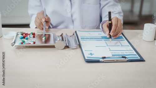 Doctor ACin white coat at desk reviewing medical form with clipboard, holding pen; tray of assorted pills and prescription bottles nearby, healthcare paperwork concept.