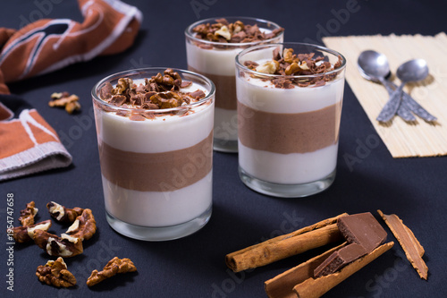 Delicious dessert cups with jelly, chocolate, and nuts on a table with utensils and cloth in the background