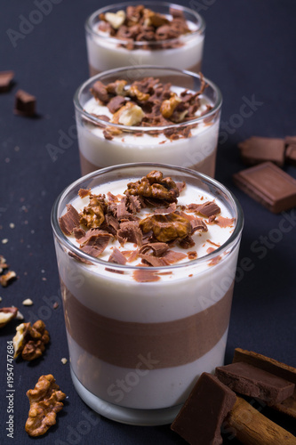 Jelly dessert cups with chocolate and nuts placed on a dark surface with extra ingredients around