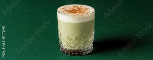 Single glass of creamy matcha latte topped with cinnamon powder on  dark green surface