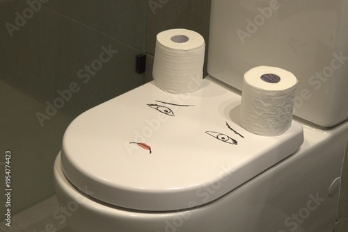 Toilet seat with rolls of toilet paper arranged in a minimal bathroom setting, representing digestive issues such as constipation, diarrhea, and gastrointestinal discomfort. Conceptual image highlight