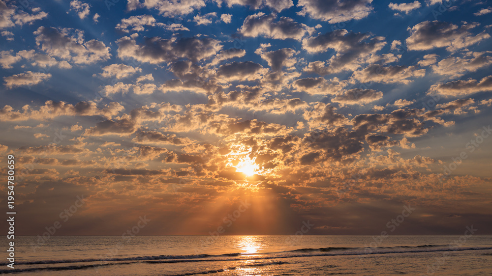 Fototapeta premium Dramatic sunrise sky with sunbeams breaking through light clouds over a sea