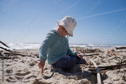 Little 4 year old girl playing with wooden sticks on a sandy beach