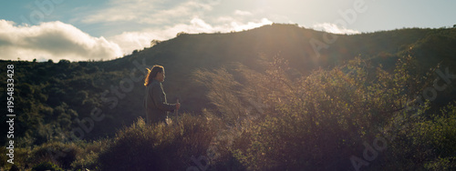 Backlit brunette woman, hair in the wind, stands on a hill in countryside. Malaga, Andalusia, Spain.