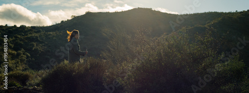 Backlit brunette woman, hair in the wind, stands on a hill in countryside. Malaga, Andalusia, Spain.