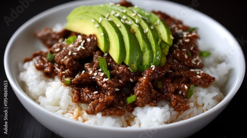 Delicious Beef Dish with Avocado Slices Served Over Steamed White Rice Topped with Sesame Seeds and Green Onions in a Bowl on Dark Background