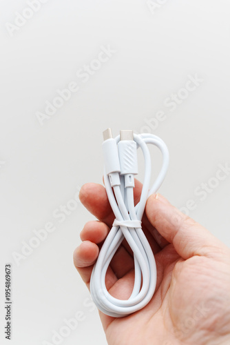 Hand holding a white charging cable against a plain background