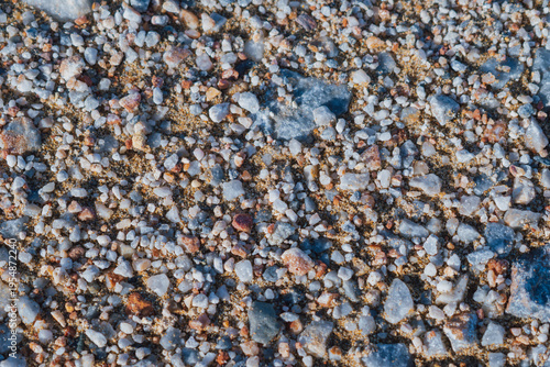 Close-up photo of a natural sea coast texture. A mix of smooth pebbles and coarse sand in earthy tones, from pearl gray to terracotta and deep graphite