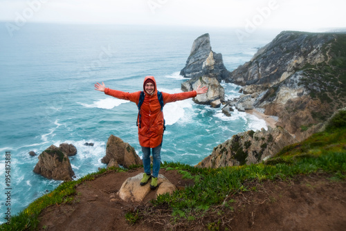 Adventurous man with open arms standing on a cliff at cabo da roca, portugal, overlooking the rugged coastline and the powerful atlantic ocean, symbolizing exploration and natural beauty