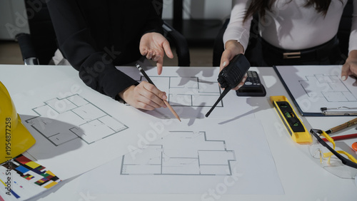 Fotografie Team of architects reviewing floor plan blueprints at office desk with tools, calculator and hard hat, discussing construction design and measurements