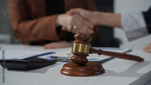 Judge gavel on desk with handshake in background, symbolizing legal agreement, settlement, or contract signing in office setting.