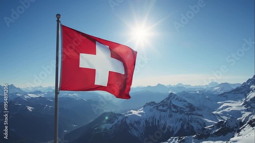A Swiss flag with a white cross on red, waving against a mountain range with snow-capped peaks under a bright sun