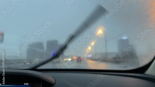 View from a car on a rainy street, wet asphalt, low visibility, urban road, adverse weather conditions, city environment