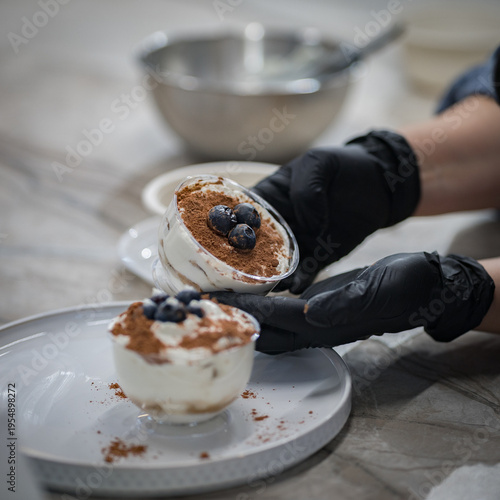 A chef wearing black gloves is preparing a creamy blueberry dessert. Close-up. Very soft focus