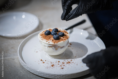 A chef wearing black gloves is preparing a creamy blueberry dessert. Close-up. Very soft focus