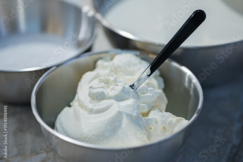 A metal bowl containing a whipped milk and cottage cheese mixture for tiramisu. Close-up. Very soft focus
