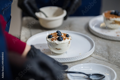 A chef wearing black gloves is preparing a creamy blueberry dessert. Close-up. Very soft focus