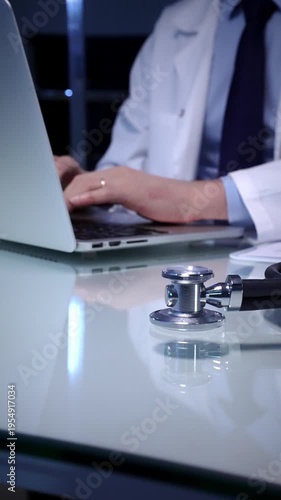 Stethoscope laying on a white reflective desk while doctor man working in clinic office. Typing on laptop and writing notes. Medicine concept