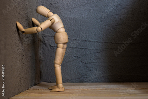 Fotografie A wooden mannequin rests its hands against a gray concrete wall