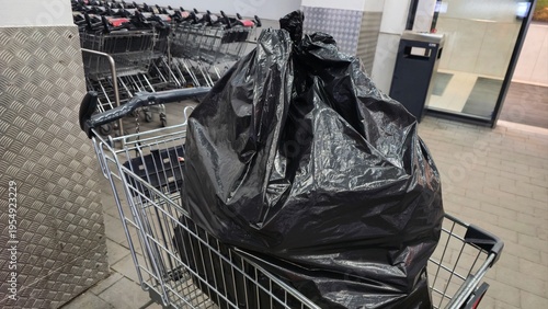 Canvastavla black garbage bags placed in shopping cart near supermarket entrance, concept of