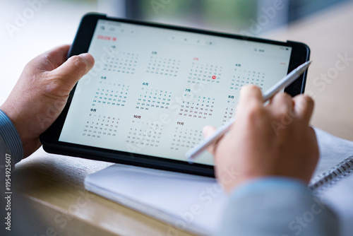 Bilde på lerret Person using a digital tablet to write and plan schedule with stylus on wooden d
