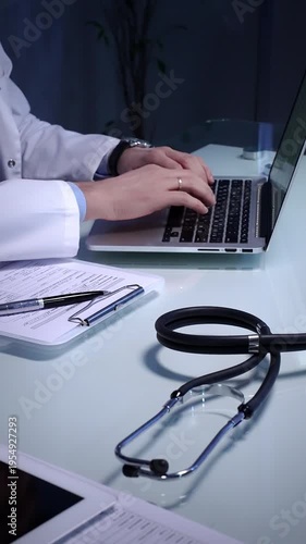 Stethoscope laying on a white reflective desk while doctor man working in clinic office. Typing on laptop and writing notes. Medicine concept