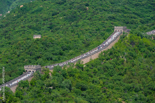 The Great Wall of China winds across the lush green mountains of Badaling under a clear blue sky.